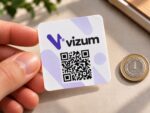 Kwadratowa naklejka z logo i kodem QR w dłoni obok monety 1 zł – przykład skali