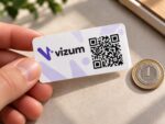 Prostokątna naklejka z logo i kodem QR w dłoni obok monety 1 zł – przykład skali